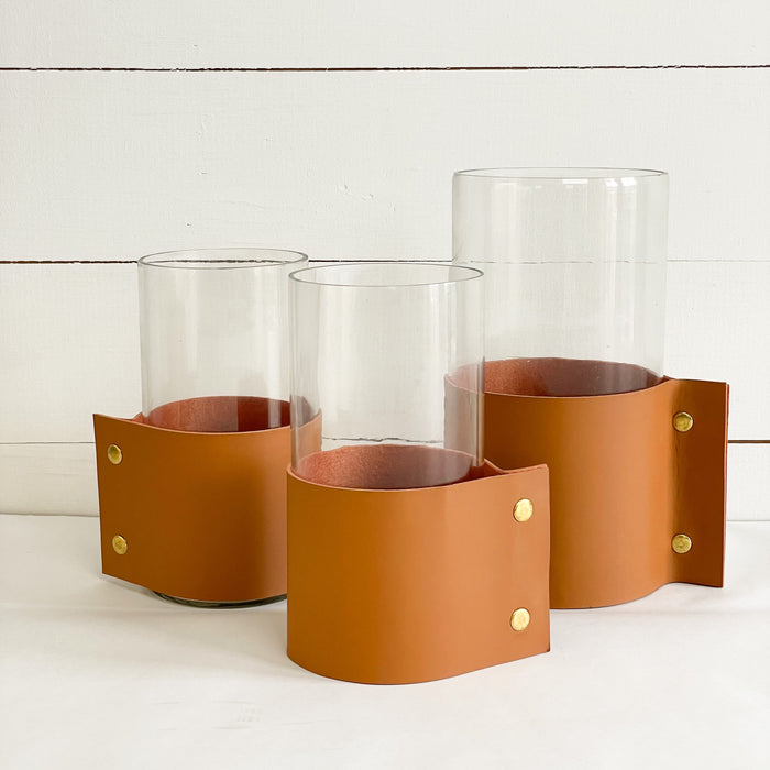 Collection of our Leather Cuff Vases shown in size medium and large. Each glass cylinder vase is wrapped with a "vegan" leather cuff and finished with brass snaps. A modern and sophisticated way to display favorite branches or blooms. Each sold separately.