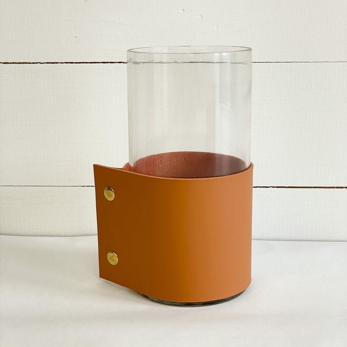 Medium vase with leather cuff measures 8" H 4" diameter. The clear glass cylinder vase is wrapped in a "vegan" leather cuff and finished with brass snaps. A modern rustic way to display your favorite branches or blooms.