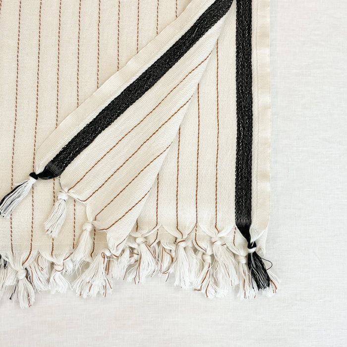 The Monterey  Towel is luxuriously oversized. Measures 37"W x 74"L. The natural cream ground has terra cotta pinstripes and a black border. Each end is finished with hand knotted tassels. Made in Turkey on traditional looms in 100% Turkish cotton.