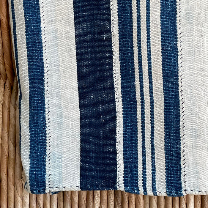 Close up of the Deep Indigo Throw showing its hand mending. This is a one of a kind vintage African textile. Hand woven in 100% cotton in a variegated indigo and natural stripe. The mending and hand stitching are part of the authenticity of this piece and should be considered part of its natural beauty. Use caution around lighter colored pieces, indigo dye may transfer to other colors. Measures 44" x 58".