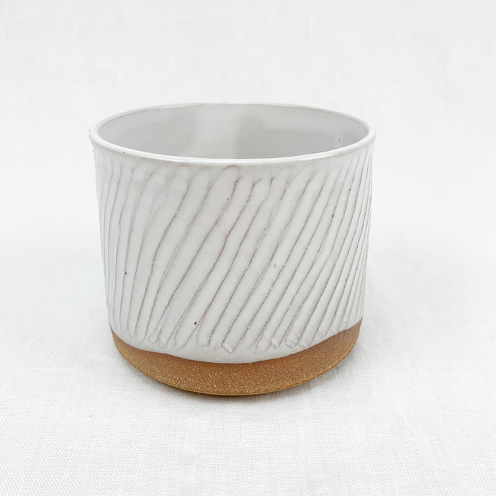 Small stoneware planter in natural clay with a white glaze. Hand carved texture.