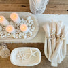 Our Whitewash Wood serving collection is hand carved from Paulownia wood. The bowl, tray and platter are all sold separately. Shown styled with white candles, natural shells and washed linens for a coastal tablescape.