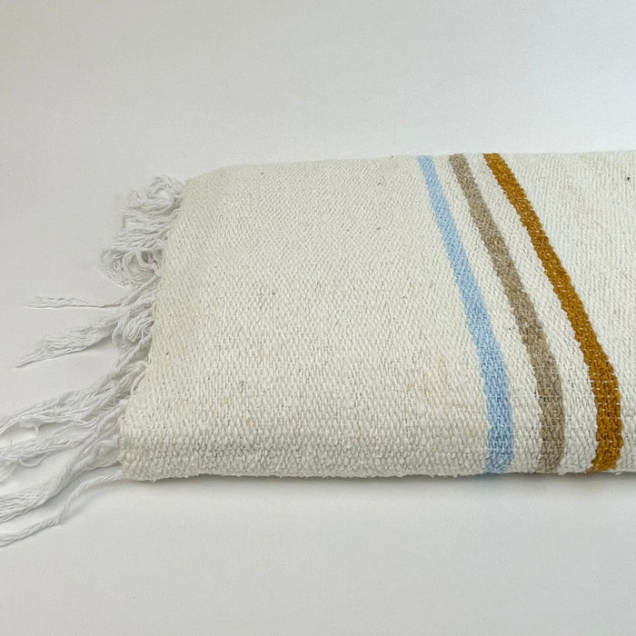 The Sunny Daze Throw is made from 100% post consumer fibers. Sustainability meets modern California style. Natural cream blanket with blue, tan and rust stripes is finished with hand twisted fringe. Measures 48" x 73"