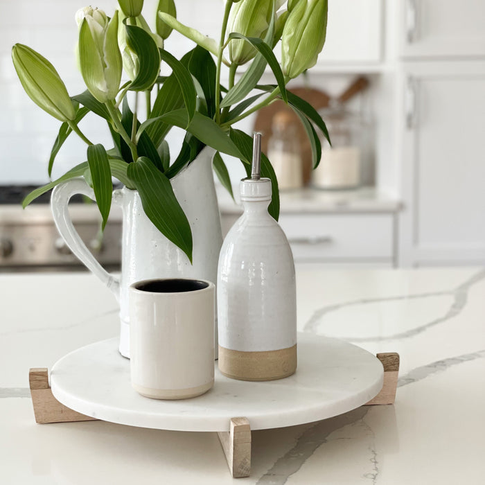Round white marble serving board/platter on natural mango wood stand. Shown with ceramic accessories, sold separately.