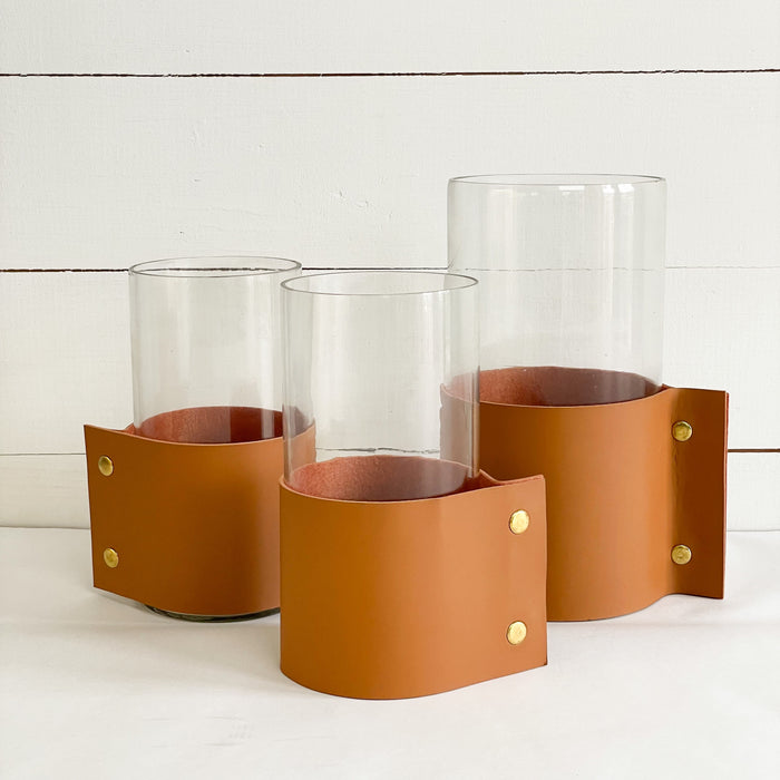 Collection of our Leather Cuff Vases shown in size medium and large. Each glass cyclinder vase is wrapped with a "vegan" leather cuff and finished with brass snaps. A modern rustic way to display your favorite branches or blooms. Each sold separately.