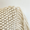 Close up of the Lola Pillow Cover. Hand made from thick natural wool yarns in a soft nubby texture. Sides are finished with long luxe fringe. Measures 14” x 20”.