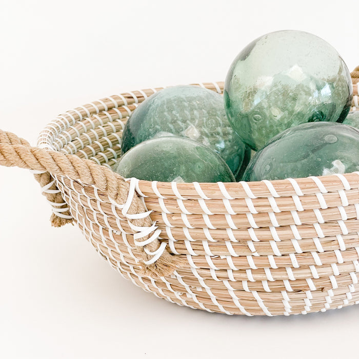 Sayulita seagrass basket is the perfect decorative accent for the boho or coastal home. The medium basket is shown here stacked with vintage glass fishing floats to create a seaside vibe. Glass floats not included.