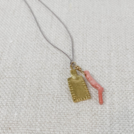 Delicate pink coral and gold tag charm necklace on grey silk cord.