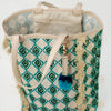 Close up view of leather handles, interior zip pocket and green and blue pom-pom charm.