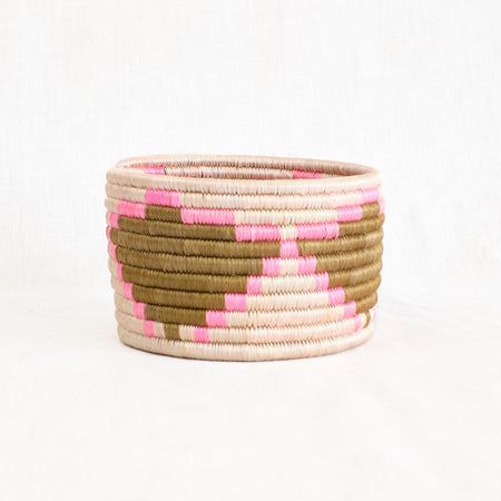 Maya basket in pink and natural tones of sisal. Hand woven using coils of sweetgrass wrapped in hand dyed sisal. Made by skilled female artisans in partnership with a non profit organization empowering women in Africa. Circular shape, measures 4" height, 5" diameter.