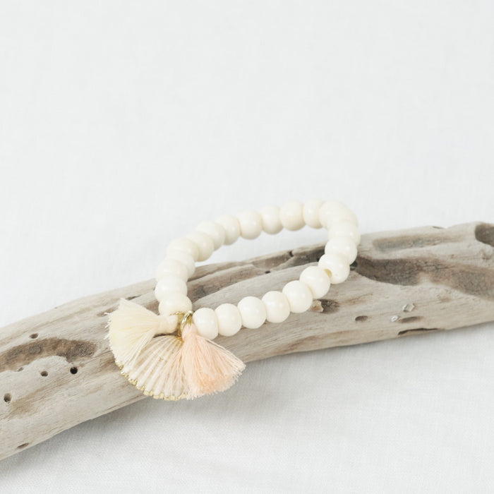 Stretch bracelet made of bone beads with a shell and mini blush tassels.