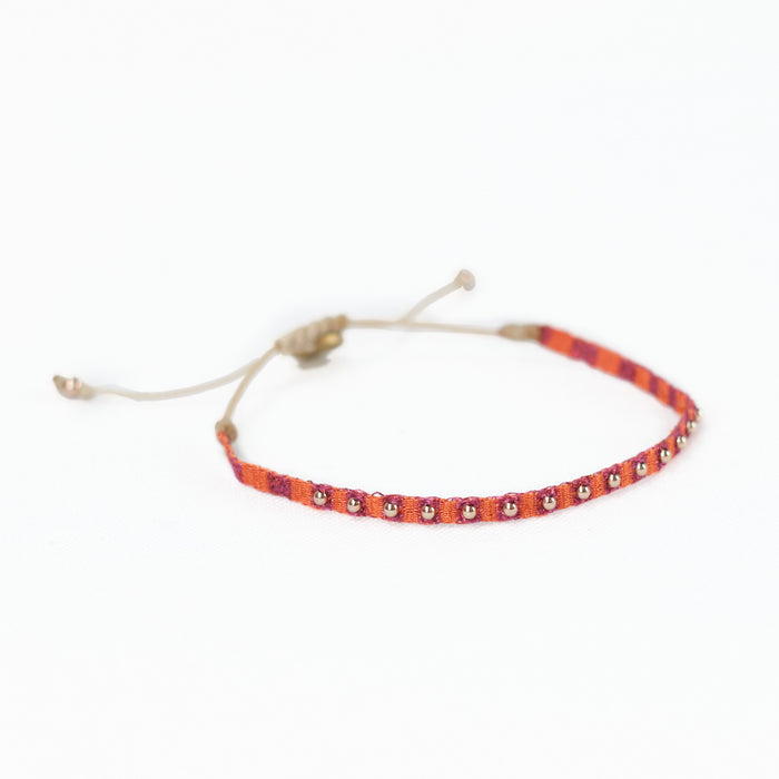 Orange and red woven friendship bracelet embellished with gold plated beads. Adjustable wax cord closure.