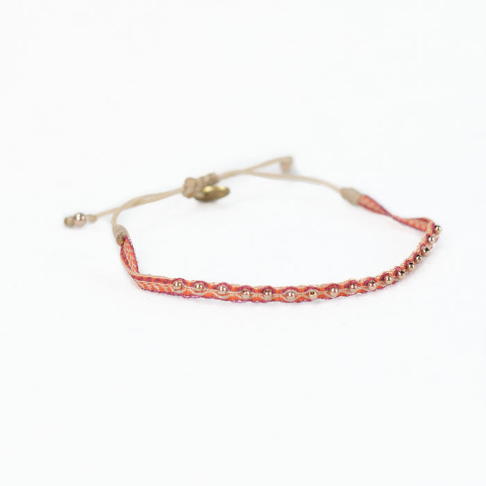 Woven friendship bracelet in orange, red and sand colors embellished with brass plated beads. Adjustable waxed cord closure.