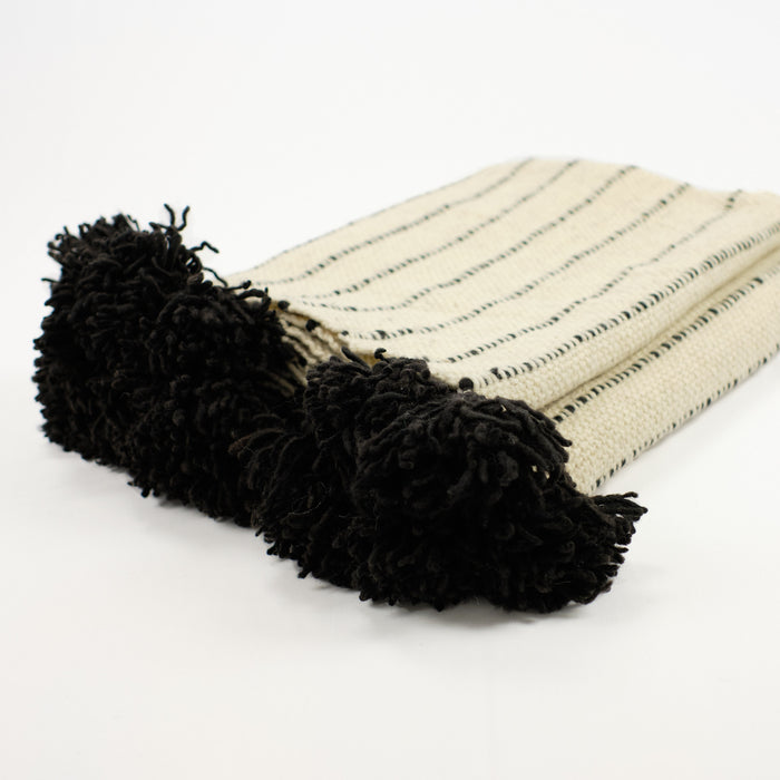 Artisan wool blanket in cream with black stripes and black pom by Treko Wool.