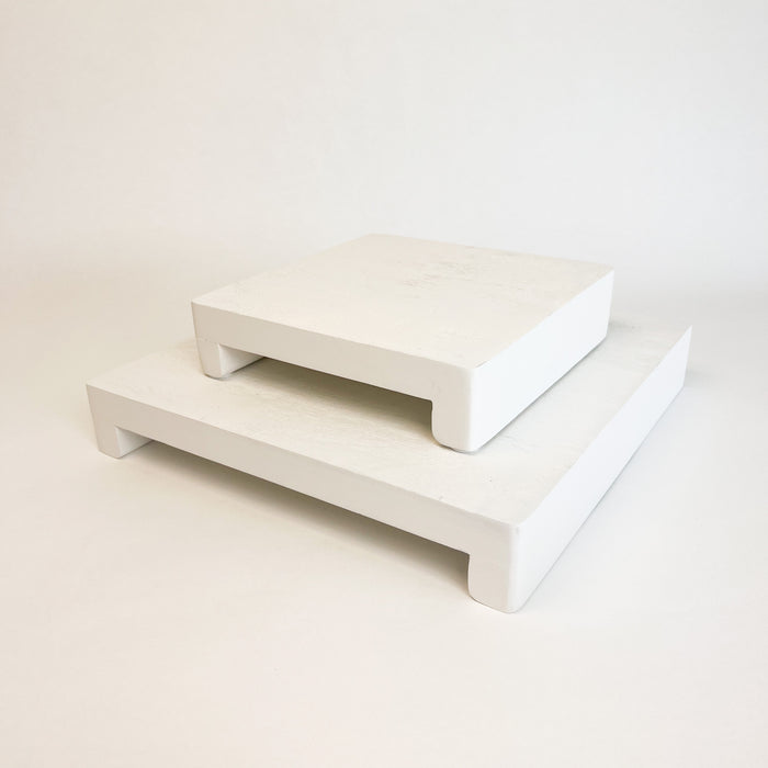 Stack of small and large white wood serving boards. Square shape made of mango wood with a glossy white finish. Each sold separately. Small 8" x 8" x2". Large 12" x12" 2".