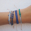 Stack of blue and green woven friendship bracelets layered on wrist. Each bracelet sold separately.