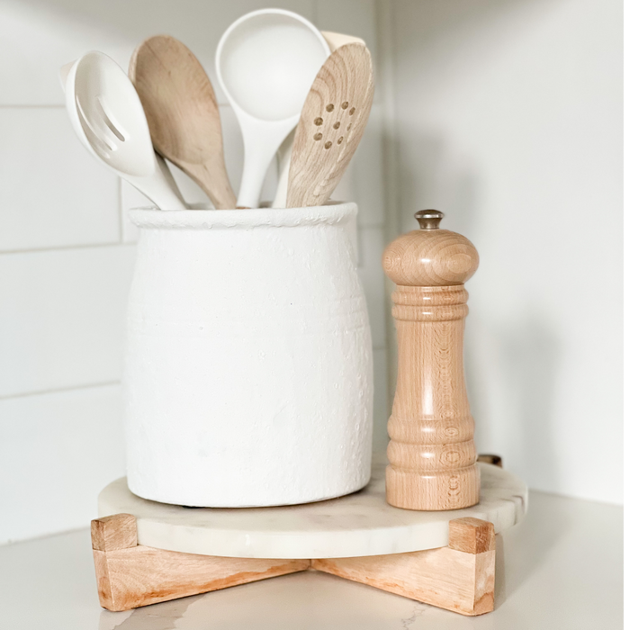 Mediterranean crock shown styled with natural wood and white kitchen utensils (not included). Hand crafted from terra cotta with a matte white lava stone finish. Coastal and modern kitchen decor. Measures 7"H 6.25" diameter.