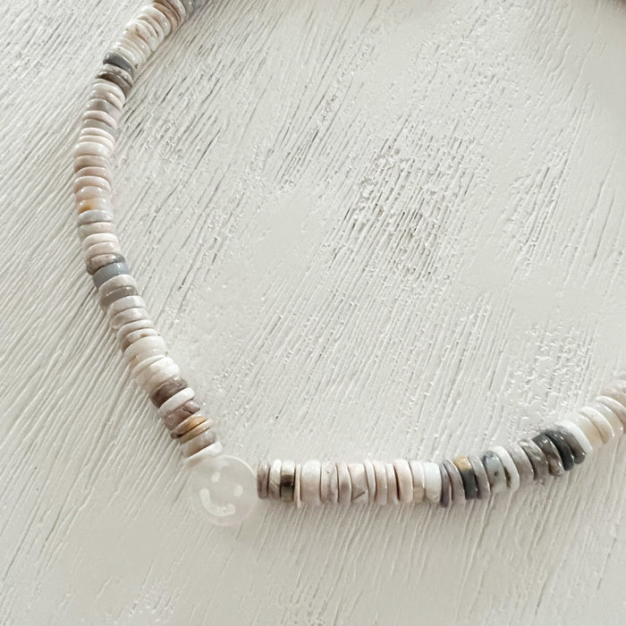 Close up of the Smile Heishi necklace featuring a hand carved mother of pearl smiley face. Handcrafted in the USA using Heishi cut Ethiopian Opal beads. A boho chic way to wear your good vibes. Length is adjustable from 14 to 16 inches.