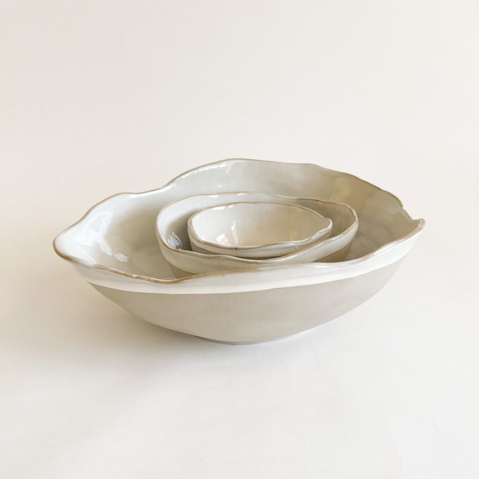 Shoreline ceramic nesting bowls. Hand shaped organic forms inspired by shells and beach pebbles. Matte grey glaze with glossy white glaze interior. Decorative accent for a coastal kitchen. Each sold separately.