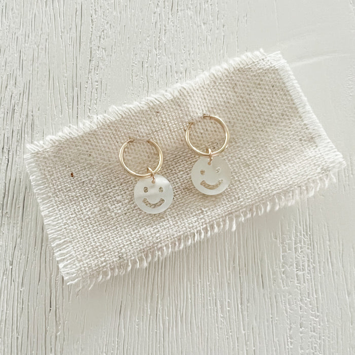 Smile hoop earrings feature a hand carved mother of pearl smiley face. Handcrafted in the USA. 12 mm infinite hoops. 14K gold filled. 