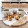 Two sunshine roly poly mugs with mini chocolate chip muffins on a wood and marble round serving board. Each item sold separately.