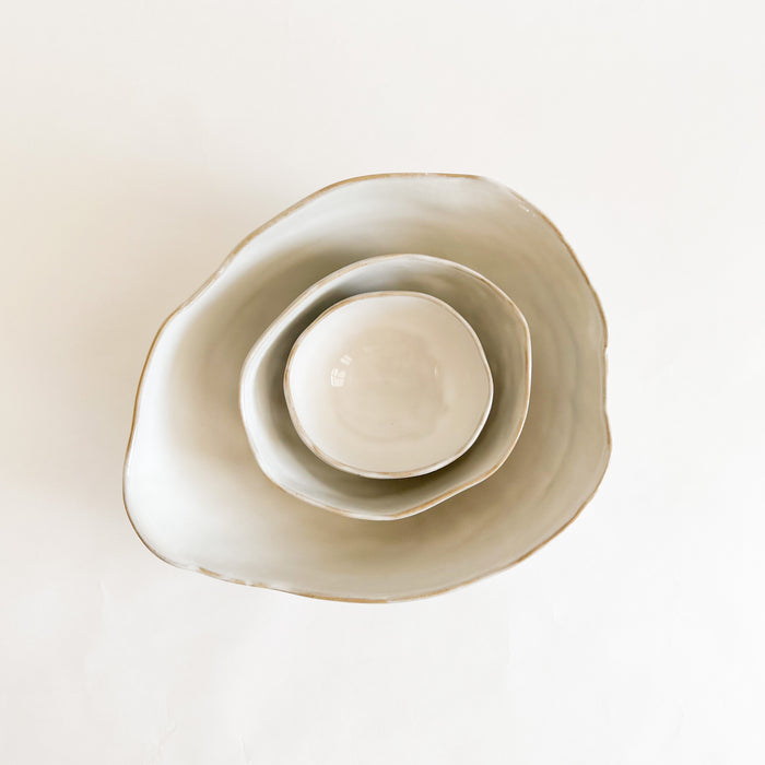 Set of Shoreline ceramic nesting bowls. Hand shaped organic forms inspired by shells and beach pebbles. Matte grey glaze with glossy white interior. Decorative accent for coastal home. Each sold separately.