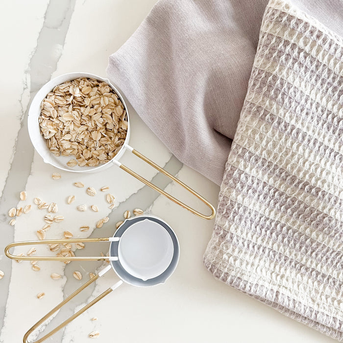 Lavender tea towels sold as a set of 2 shown with our brass and white enamel measuring cups. Each sold separately.