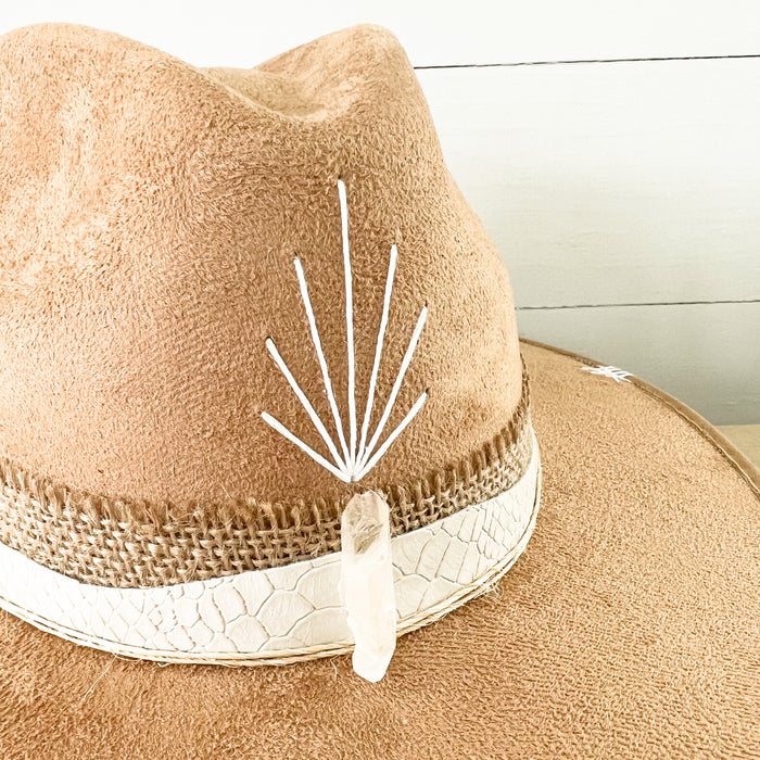 Close up detail of the front of the Sparkles Hat featuring a clear crystal and hand stitched symbols. Finished with a burlap and white snakeskin strap.
