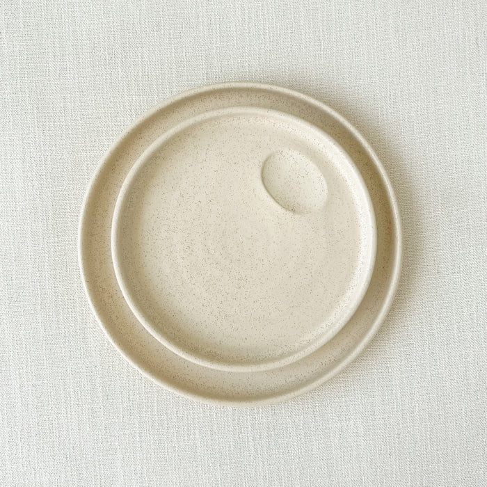 Mesa stoneware plates. Small batch stoneware made in Portugal. Each plate features a hand formed dimple for creating an artful presentation with a sauce or dressing. Finished in a creamy matte white glaze perfect for the modern table. Small and large plate shown. Each sold separately.