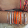 Stacks of orange, coral and hot pink woven friendship bracelets shown layered on the wrist. Each sold separately.