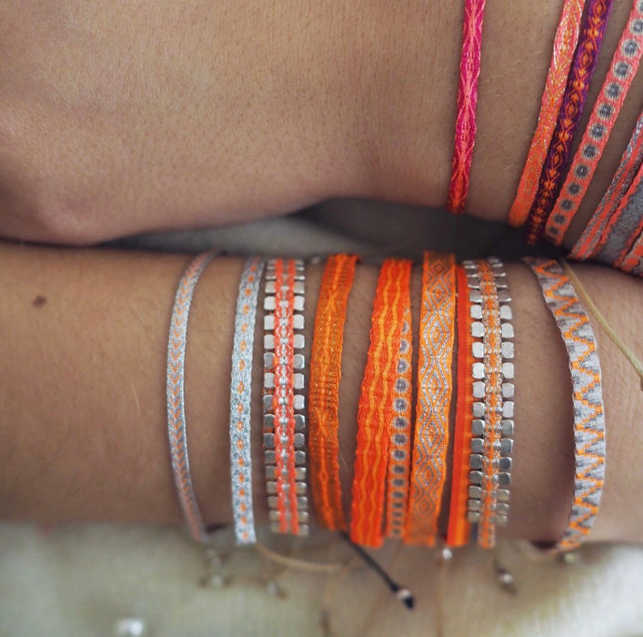 Stacks of orange, coral and hot pink woven friendship bracelets shown layered on the wrist. Each sold separately.