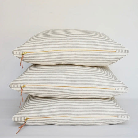 Stack of 3 Palma stripe linen pillows. Each sold separately. Linen pillow cover in 1/2" oatmeal and ivory stripes finished with a brass zipper and leather pull. 27" square. Down insert included.