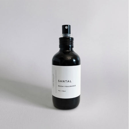 Bottle of Santal Room Fragrance by Lightwell Co. 4 oz. opaque black glass bottle with modern white label. Fragrance notes: woody and musky with notes of ambergris, sandalwood and cedar. 