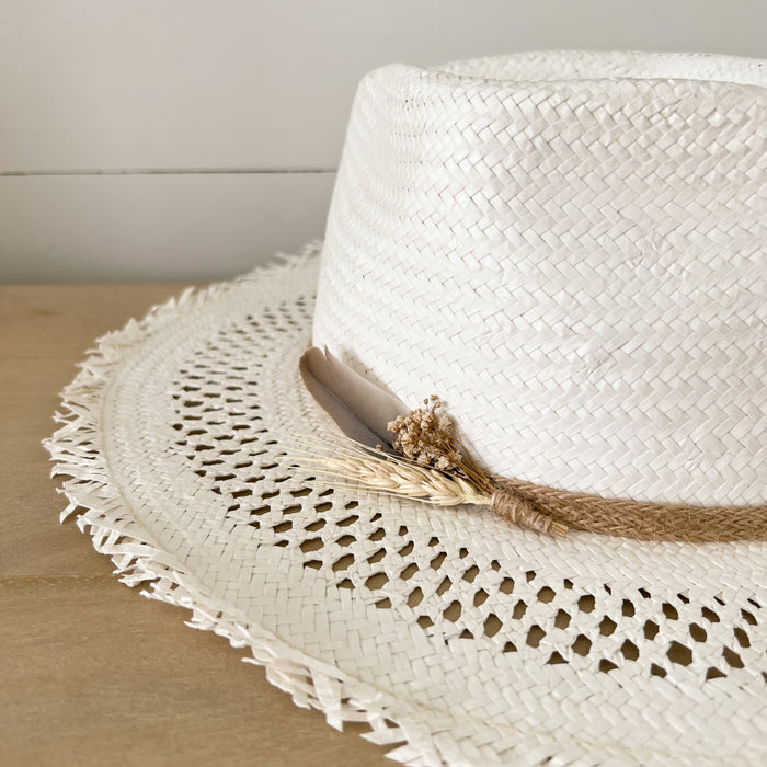 Summer State Straw Hat in white straw with fringe edges. Decorated with natural braided jute, a small sprig of dried wild flowers and a small feather. 