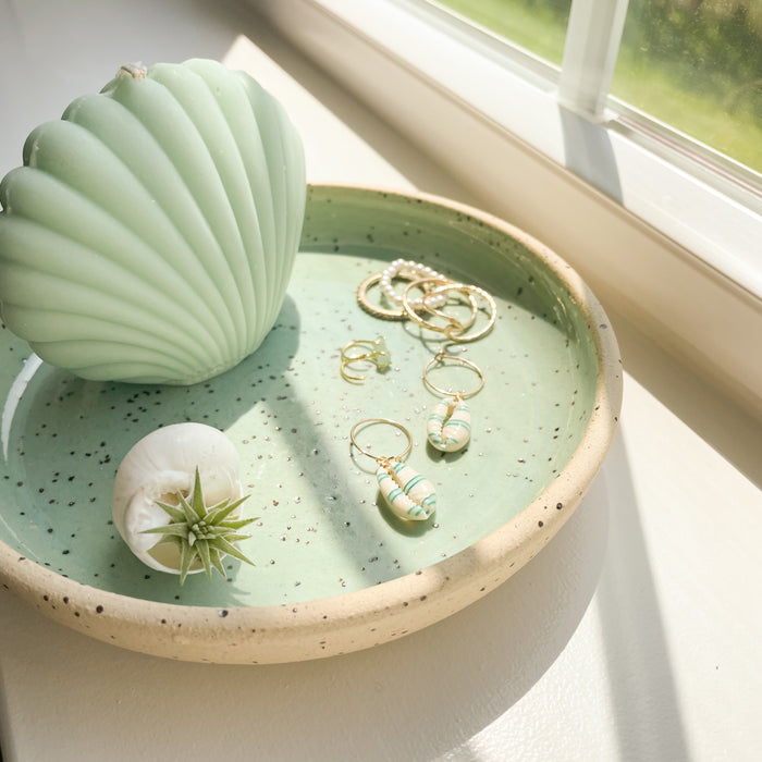 Momo dish shown in the seafoam glaze holding jewelry and shell candle (items not included). Hand crafted by Tamiko Claire in Hawaiii. Measures 6.25" diameter 1" height.