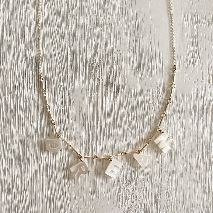 The Dream necklace features hand carved mother of pearl letters on a 14K gold filled chain. A gentle reminder to always dare to dream. A perfect gift for the graduate. Adjustable length of 16 to 18 inches.