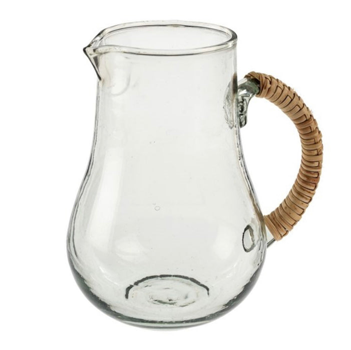 Isla glass pitcher made of clear mouth blown glass with a hand wrapped rattan handle. 7" height. 4.5" diameter at base. Artisan made.