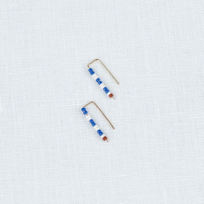 Small beaded earrings in a blue and white stripe pattern with a tiny dark red bead to finish. Blue & white earrings by Alice Rise.